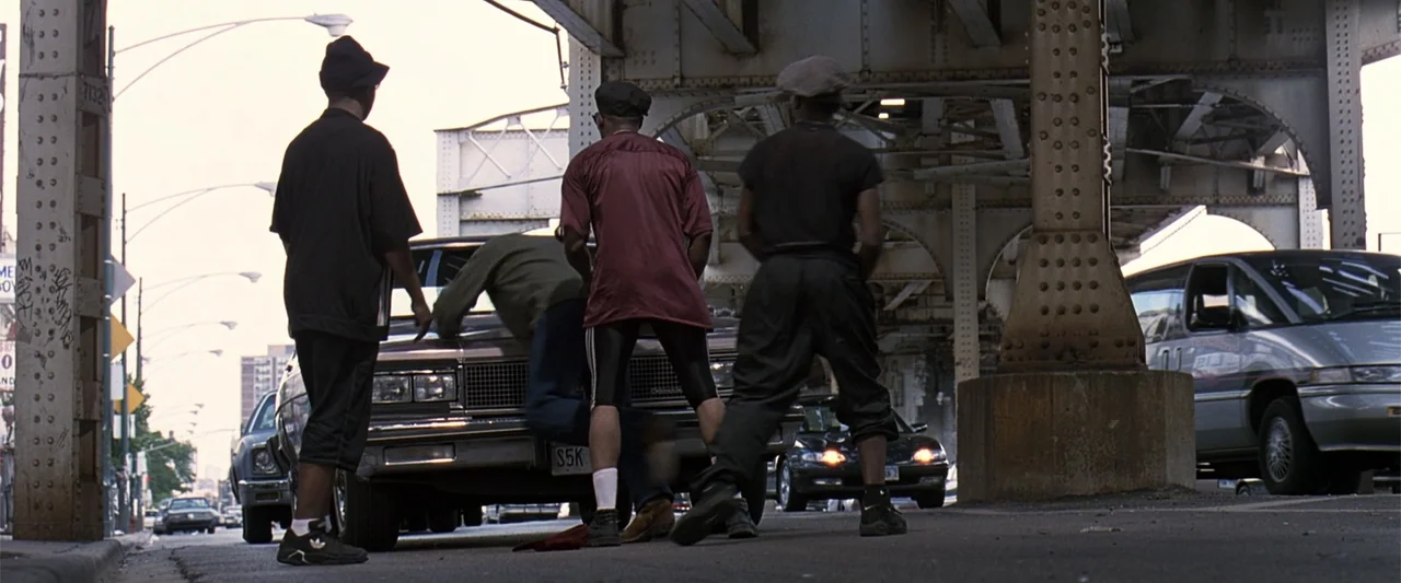 A Family Thing (1996) movie still: fullbody — An urban street beneath a large iron and concrete elevated train track. Several men gather around a…
