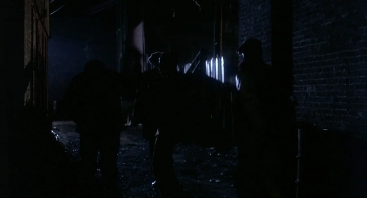 Cooley High (1975) movie still: fullbody — An urban alleyway features dark brick walls and a damp ground surface at night. Three figures in dark…
