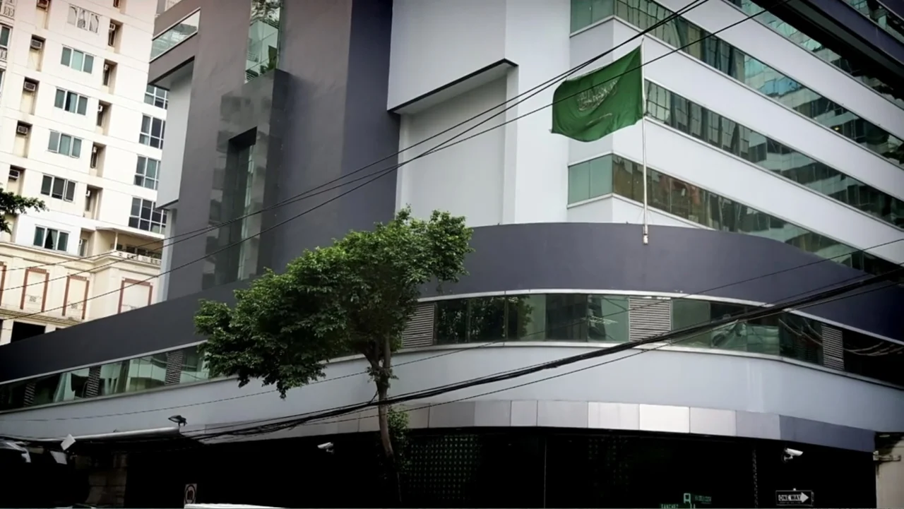 Escape From Saudi (2019) movie still: establishing — A modern commercial building features white and dark grey panels with horizontal windows and a…