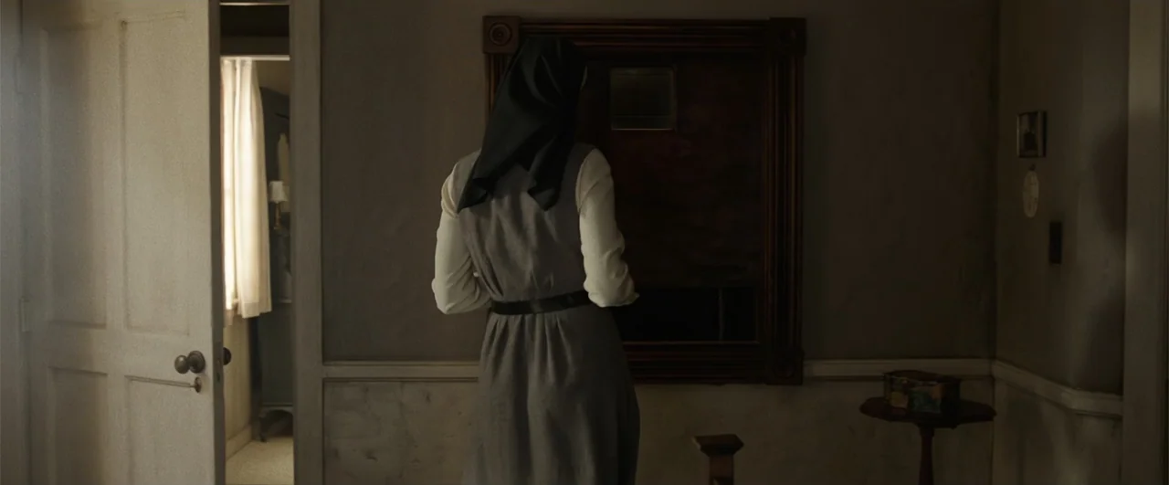 Annabelle: Creation (2017) movie still: medium — A dimly lit room features a nun facing a wooden panel on the wall. An open doorway in the…