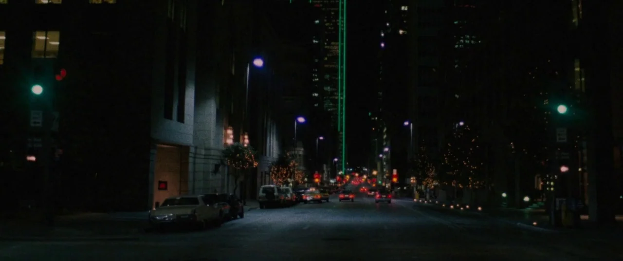 The Old Man & The Gun (2018) movie still: establishing — A dark city street at night is flanked by tall office buildings and parked cars. Several…