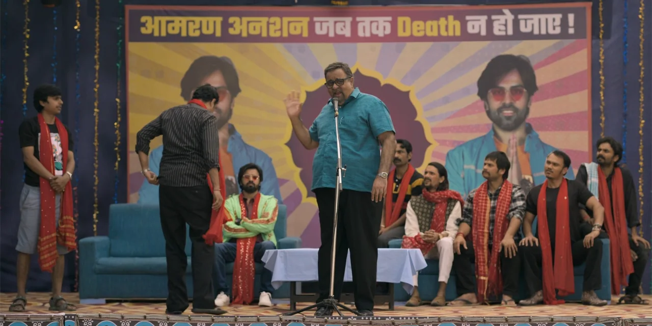 Dry Day (2023) movie still: fullbody — A outdoor stage features a large banner with Hindi text and a microphone stand. A man in a blue shirt…