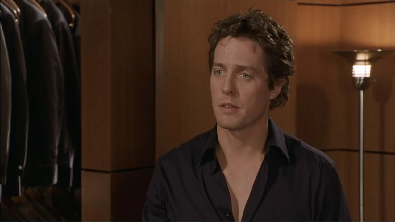 Two Weeks Notice (2002) movie still: medium — A high-end boutique interior features dark wood paneling and hanging garments on display. A man stands…