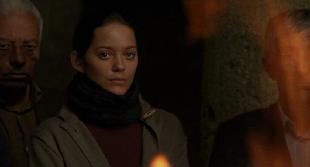 Furia (1999) movie still: medium — A dimly lit interior space features three people huddled together in low light. The central female subject stands…