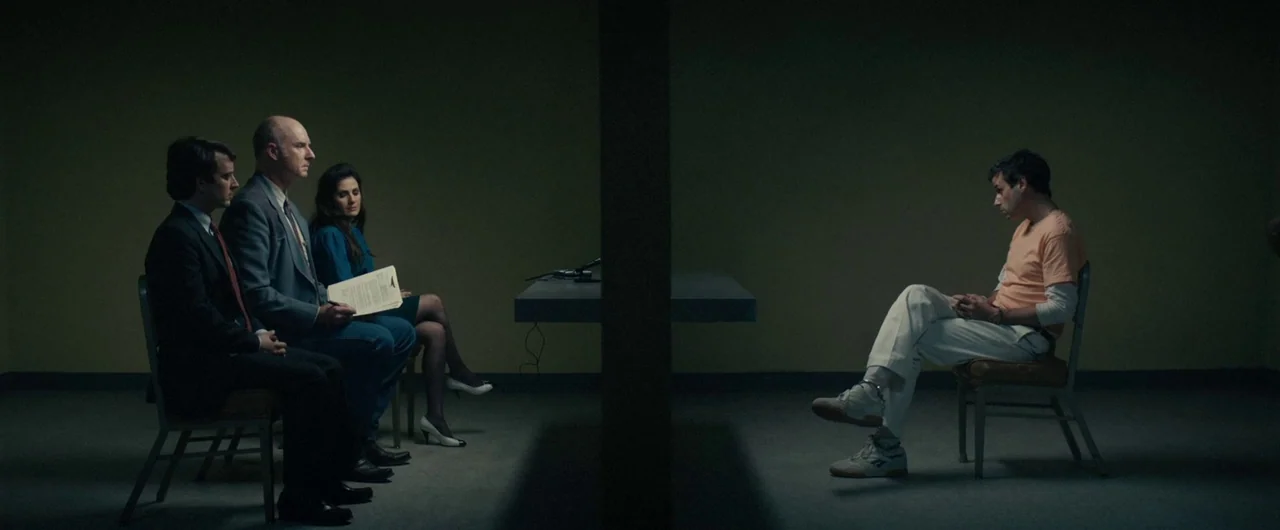 No Man of God (2021) movie still: wide — A stark interrogation room has drab green walls and a single central support pillar. Three people sit on…