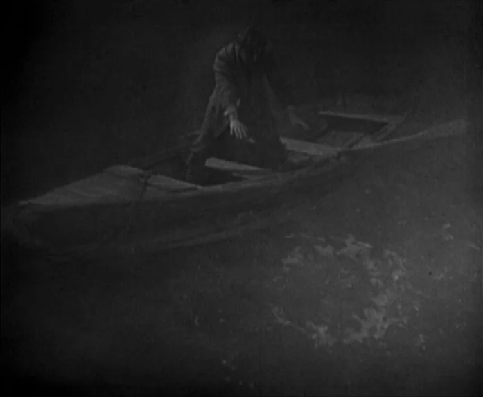 Sunrise (1927) movie still: wide — A wooden rowboat floats on a dark, still body of water at night. A lone man crouches inside the boat while…