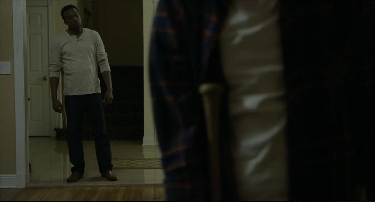 Freedom (2024) movie still: medium — A residential hallway features beige walls and an open doorway leading into a room. A man stands in the…