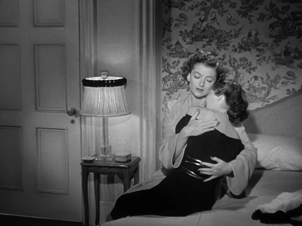 The Best Years of Our Lives (1946) movie still: medium — A room with patterned wallpaper and a closed door next to a small lamp table. One woman…