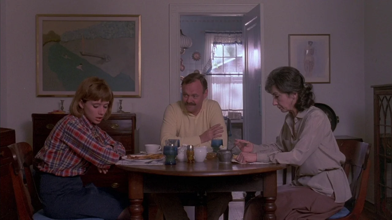 Baby It’s You (1983) movie still: medium — A modest dining room features white walls, framed art, and a round wooden table. A young woman and an…