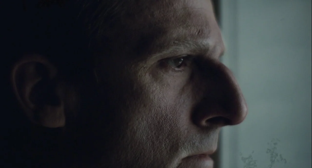 Foxcatcher (2014) movie still: closeup — A dimly lit interior space with a person in shadows. The subject turns their face toward a source of light.