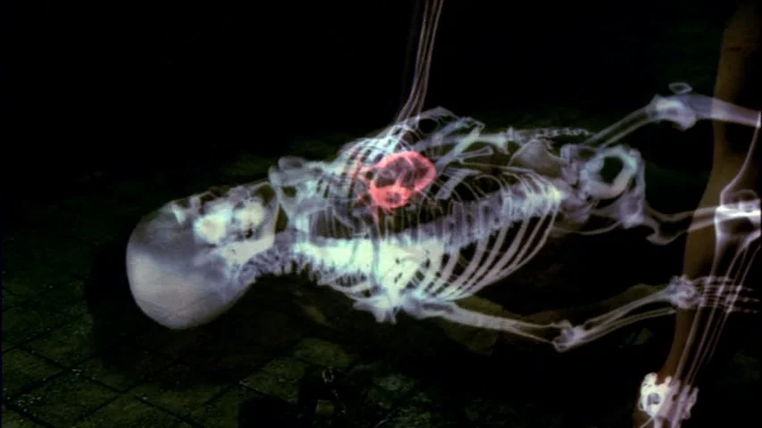 Save The Green Planet! (2003) movie still: medium — A dark, tiled interior space holds the glowing projection of a human skeleton. The chest cavity…