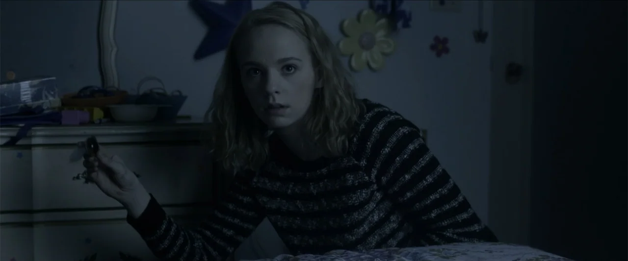 The Hollow Child (2018) movie still: medium — A dimly lit bedroom features floral wall decals on a dark blue wall surface. A young woman in a…