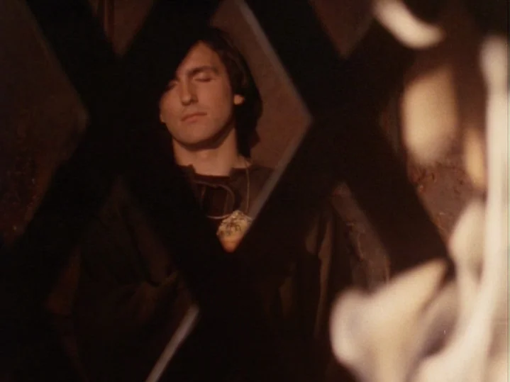 The Magic Flute (1975) movie still: medium — A dark stone cell features a heavy dark metal grate in the foreground. A man rests his head against the…