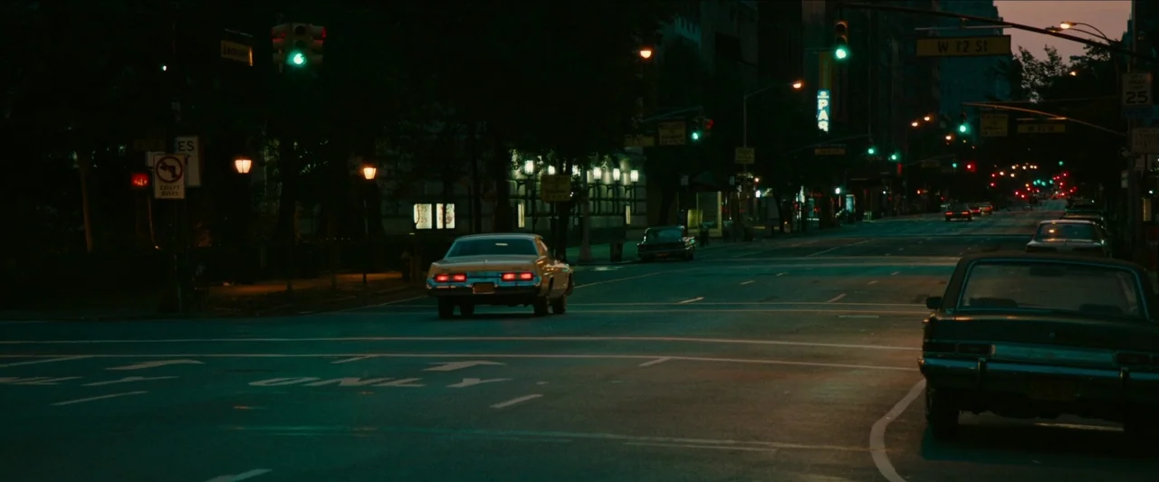 Wonderstruck (2017) movie still: wide — A quiet urban intersection at night features vintage American cars idling in the dark. Road markings are…