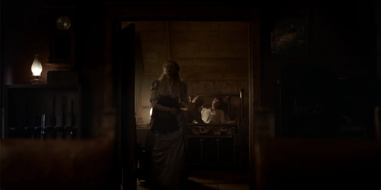 Deadwood: The Movie (2019) movie still: medium — A dark wooden bedroom with a brass bed frame and period wall clocks. A woman stands in the doorway…