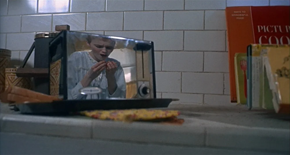 Rosemary’s Baby (1968) movie still: closeup — A kitchen counter features white tiled walls and a chrome toaster reflecting a person. A woman with…