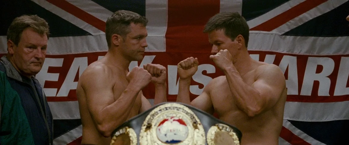 The Fighter (2010) movie still: medium — Two professional boxers stand face-to-face before a large, draped British Union Jack banner. A championship…
