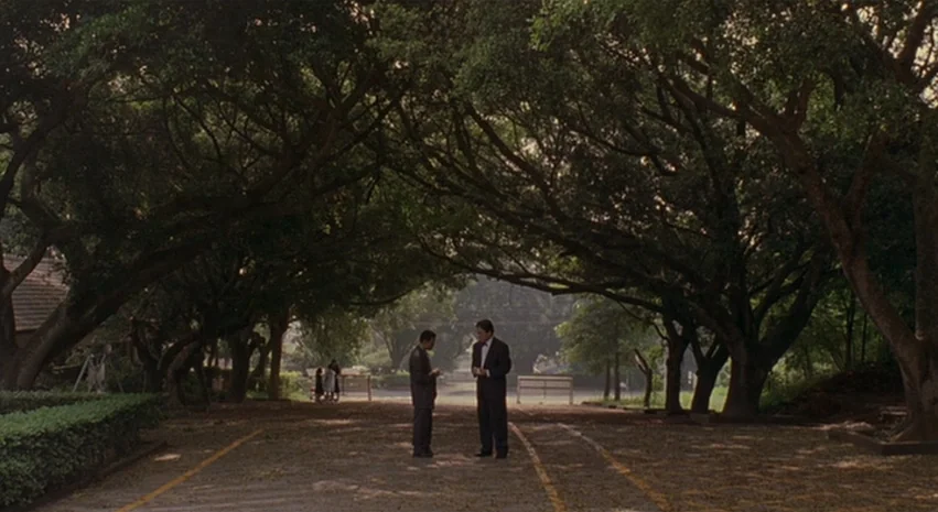 Yi-Yi (A One and A Two) (2000) movie still: wide — A tree-lined road is flanked by large mature trees forming an overhead canopy. Two men stand in…