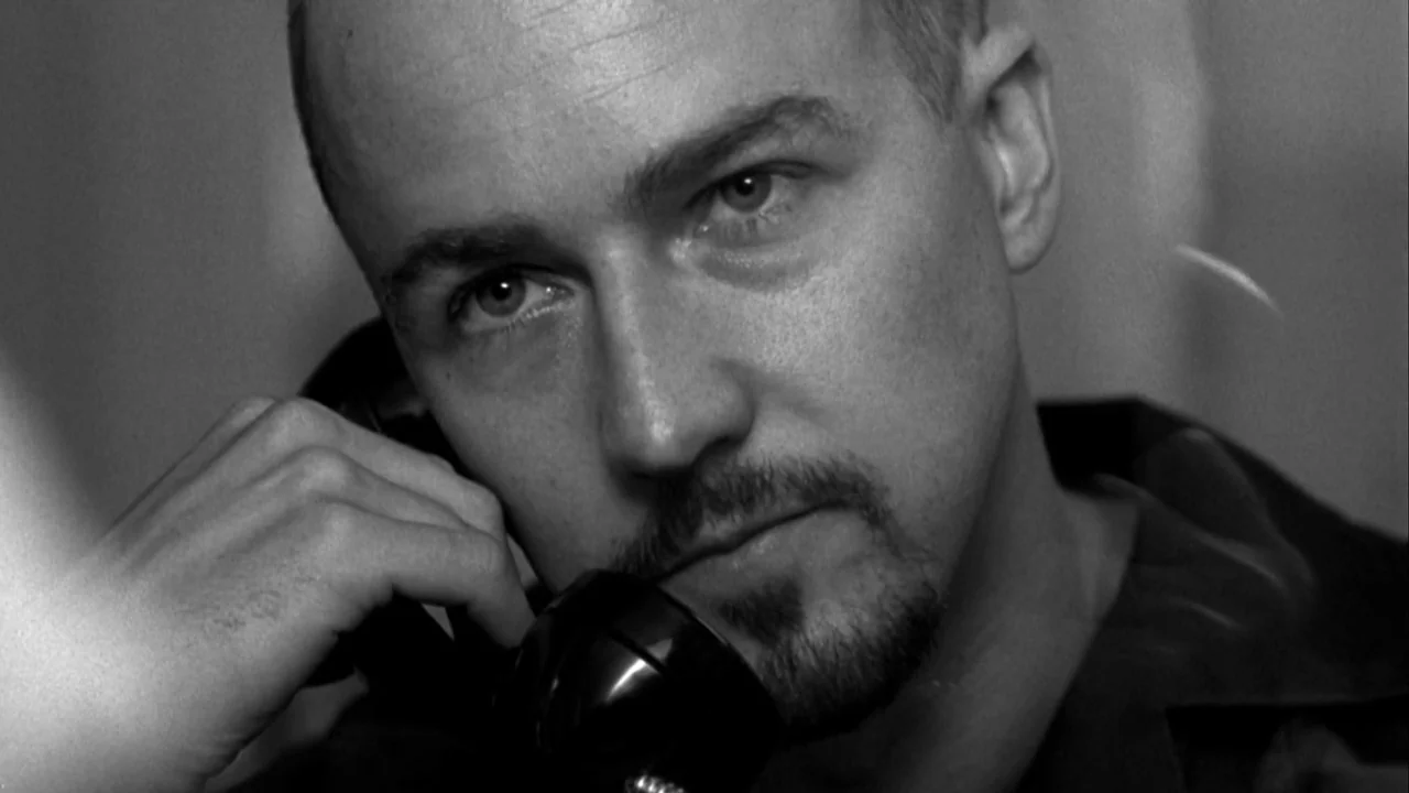 American History X movie still: closeup — A man speaks on a black landline telephone inside a confined space. He holds the receiver against his ear…