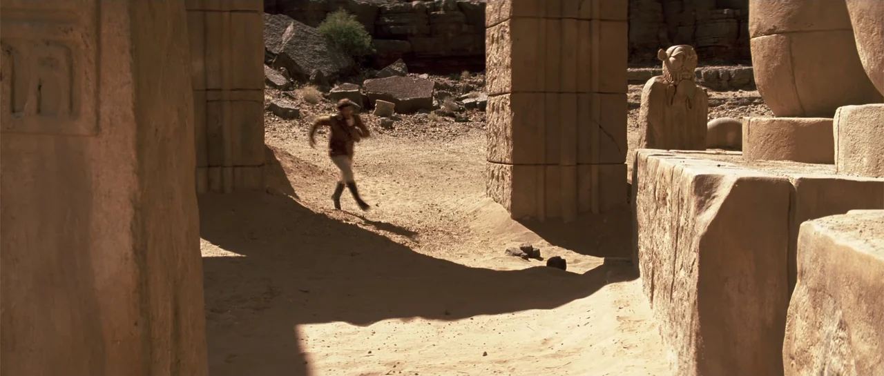 The Mummy (1999) movie still: wide — An arid, sun-baked site features weathered stone pillars and ancient sandstone statues. A man in a leather…