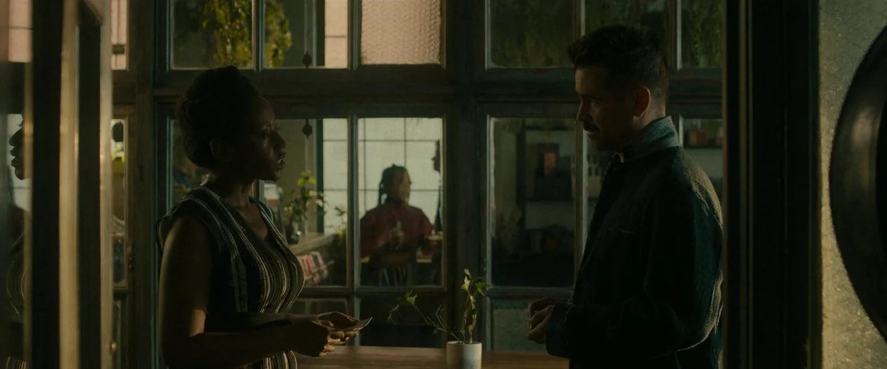 After Yang (2021) movie still: medium — A dimly lit room features a wall of large, multi-pane glass windows looking outside. A man and woman stand…