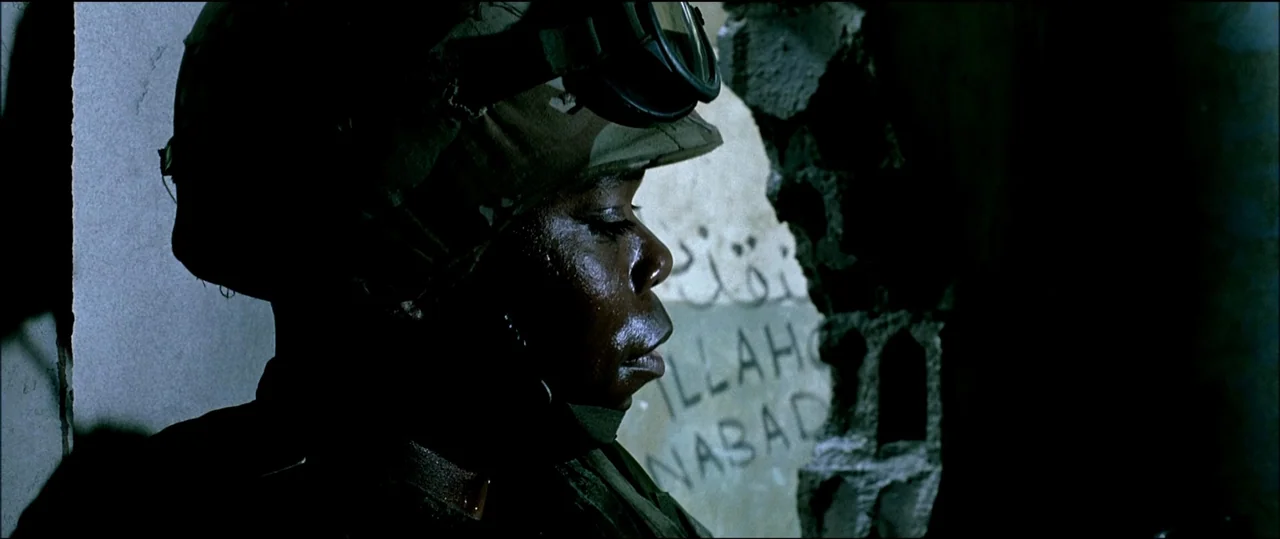 Black Hawk Down (2001) movie still: closeup — A soldier in combat gear leans against a crumbling wall in a dark structure. The wall features…