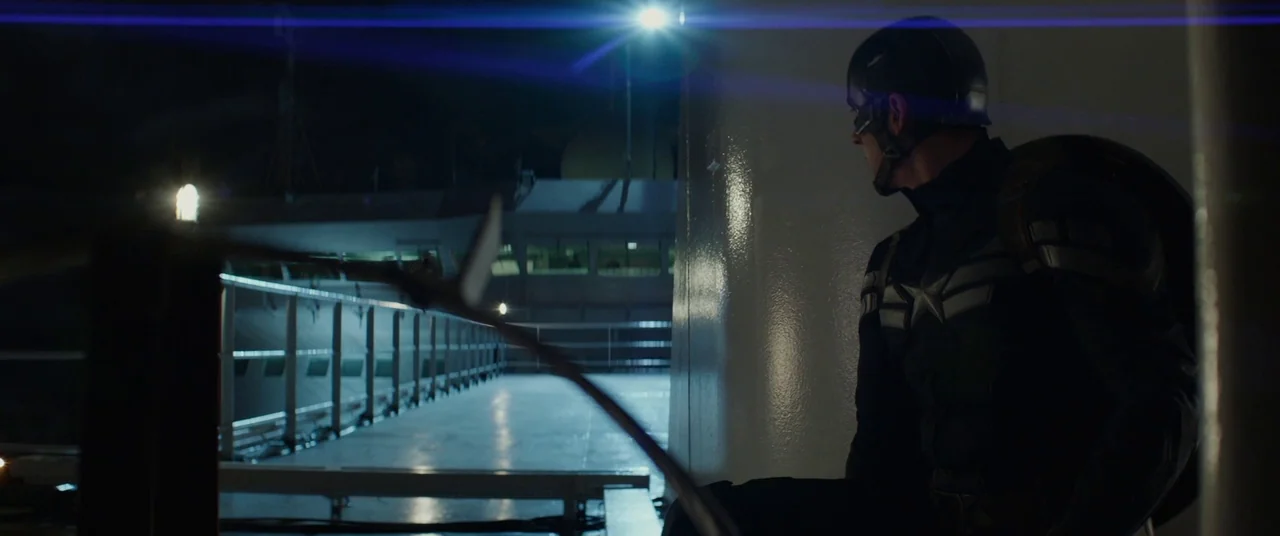 Captain America: The Winter Soldier (2014) movie still: medium — A dark, metallic deck of a large vessel at night features an illuminated bridge. A…
