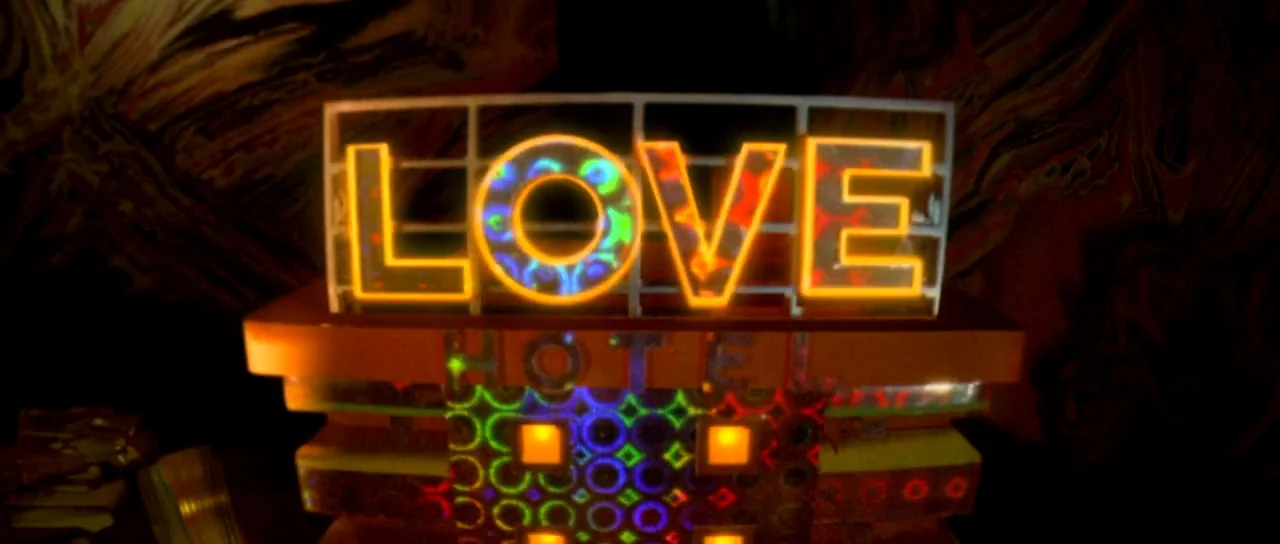 Enter The Void (2009) movie still: closeup — A close-up miniature model of a hotel sign with illuminated neon text spelling LOVE. The background…