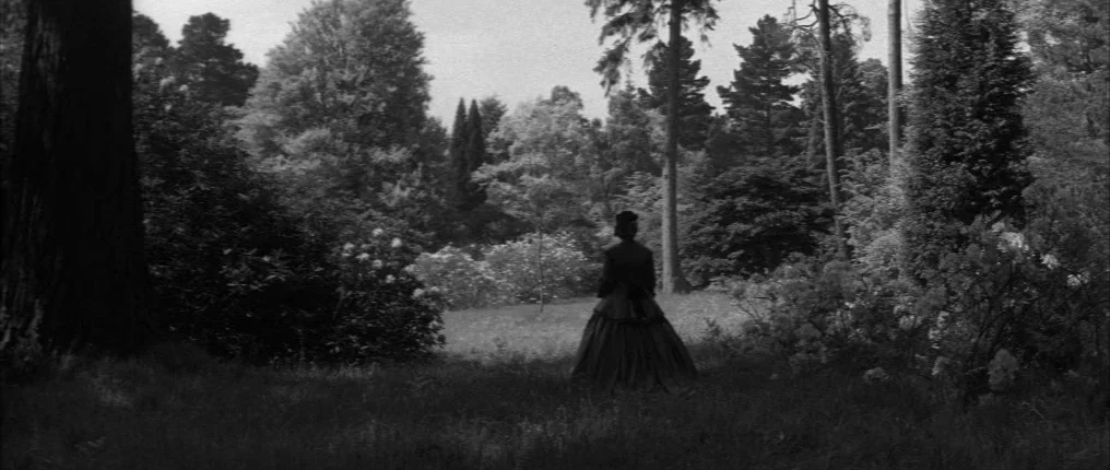 The Innocents (1961) movie still: wide — A sprawling lawn surrounded by tall mature trees and shrubs under an overcast sky. A lone woman wearing a…