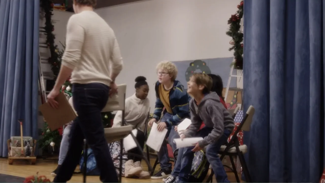 A Christmas Break (2020) movie still: medium — A room decorated for Christmas with blue curtains and a small tree in background. An adult man walks…