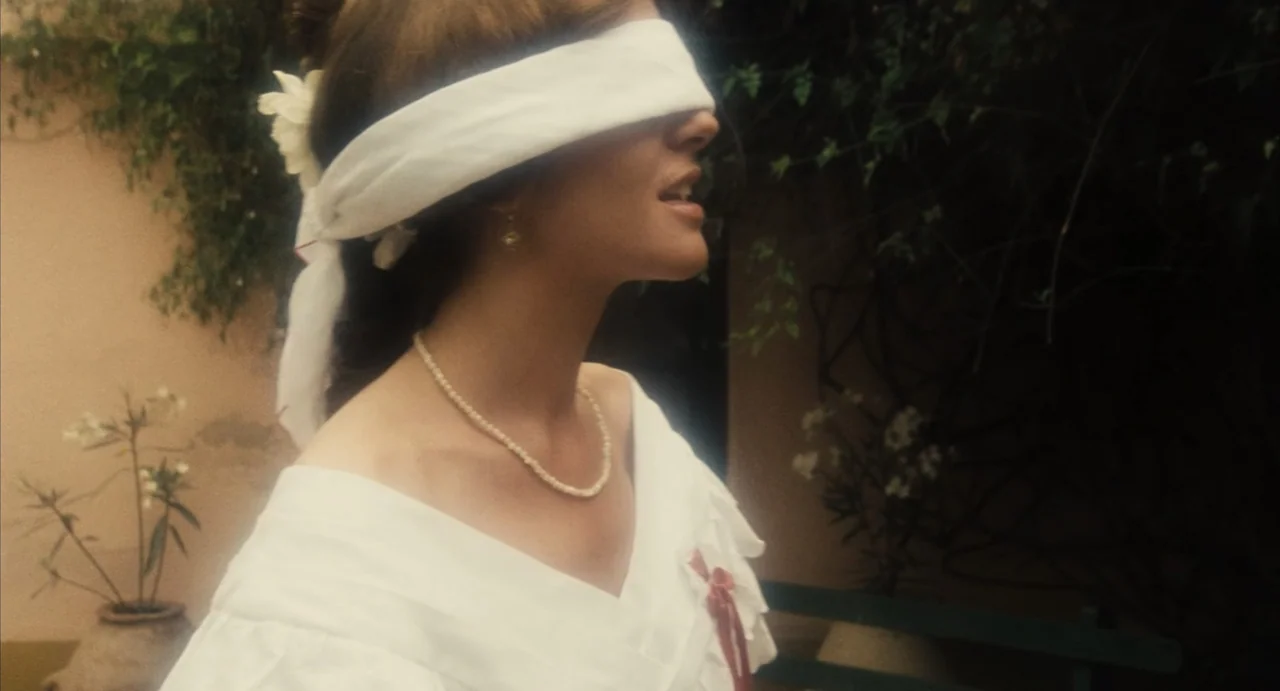 Camila (1984) movie still: closeup — A garden setting features a light-colored wall covered by creeping vine branches. A woman wearing a white…