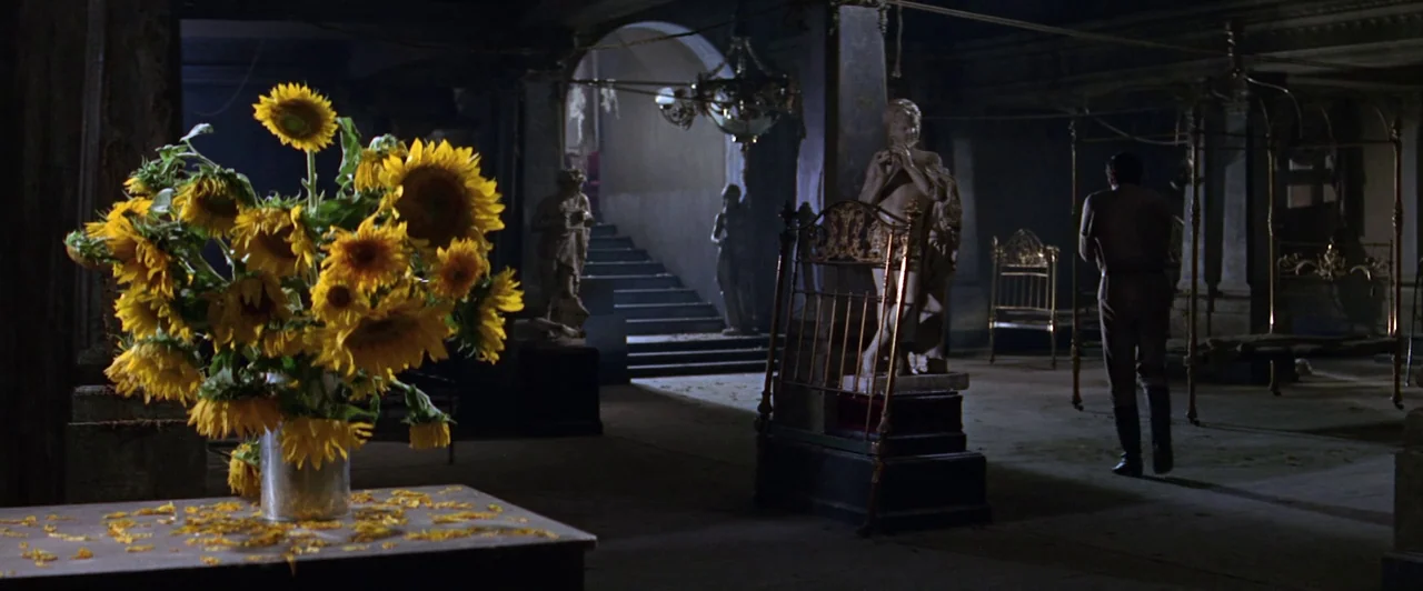 Doctor Zhivago (1965) movie still: wide — A spacious, dimly lit interior features classical statues, ornate metal bed frames, and stairs. A lone man…