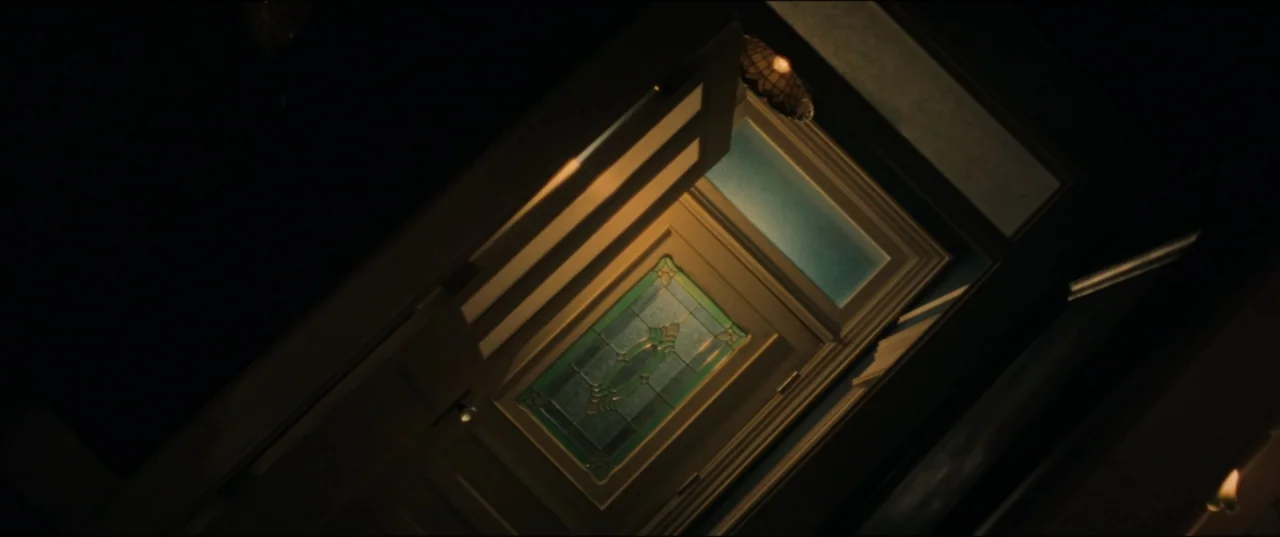 Vicious (2025) movie still: medium — A wooden interior door with decorative stained glass panels is ajar in darkness. Warm light spills from an…