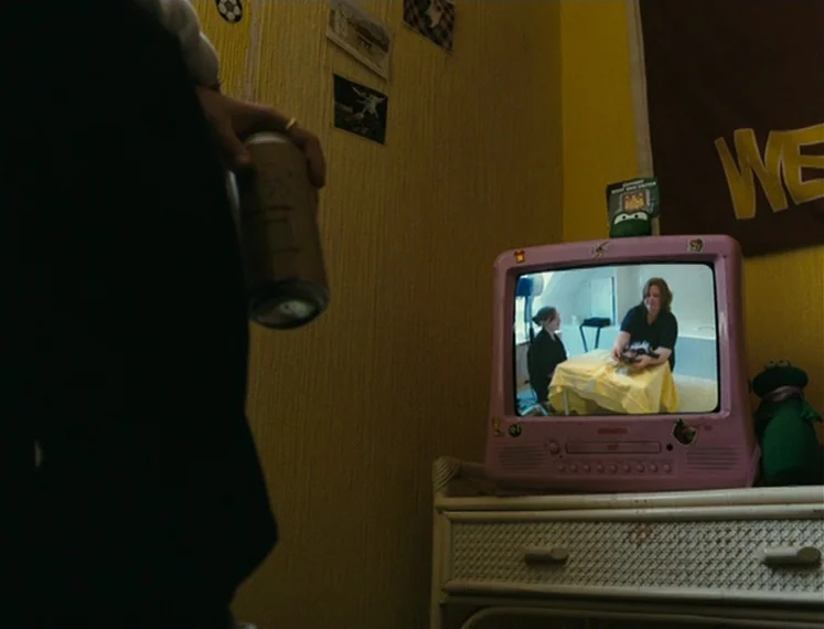 Fish Tank (2009) movie still: medium — A yellow-walled room features a small pink television displaying another internal scene on screen. A person…