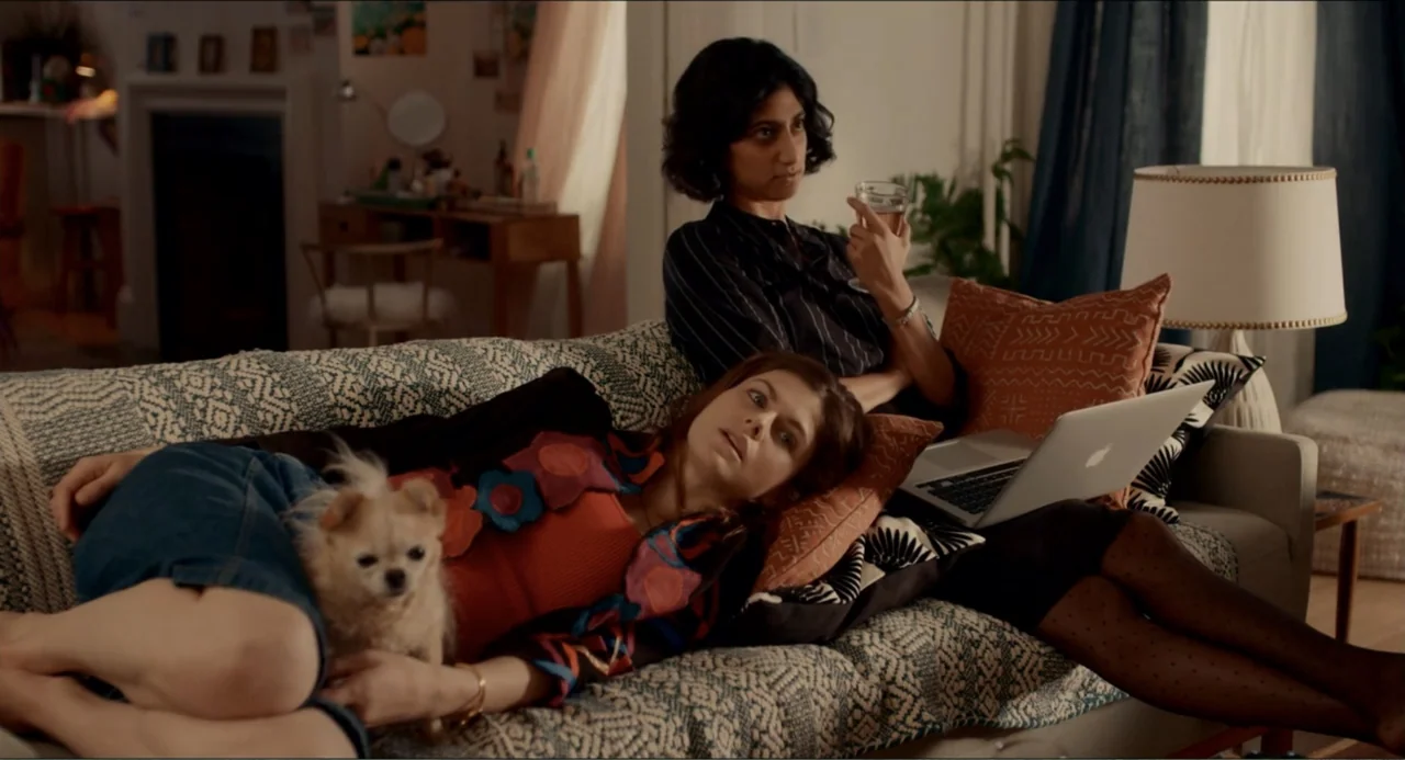 Can You Keep a Secret? (2019) movie still: medium — A furnished living room with a patterned sofa, accent pillows, and a laptop nearby. Two women…