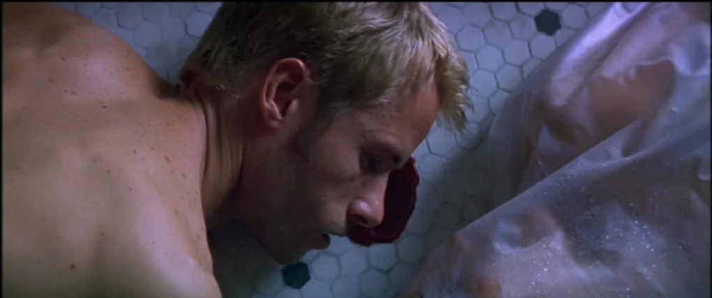 Memento (2000) movie still: closeup — The frame shows a tiled floor made of small white hexagonal tiles with dark accents. A shirtless man with…