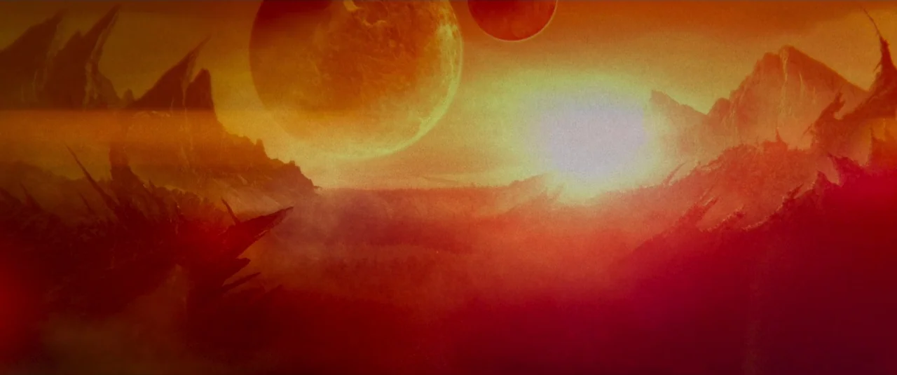 Mandy (2018) movie still: establishing — An arid, alien planet features sharp, rocky peaks under a hazy, glowing orange sky. Two large planetary…