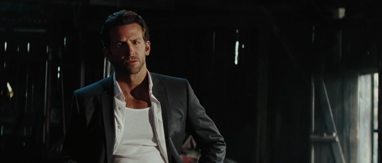 The A-Team (2010) movie still: medium — A man stands inside a dark, wooden structure with light streaming through a side window. He stares directly…