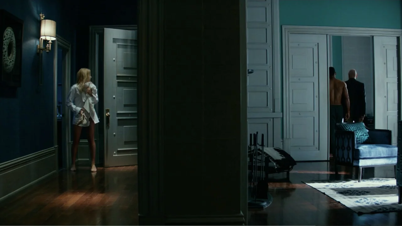 Focus (2015) movie still: wide — A spacious apartment features navy blue walls, high ceilings, and light-colored paneled doors. One woman remains in…