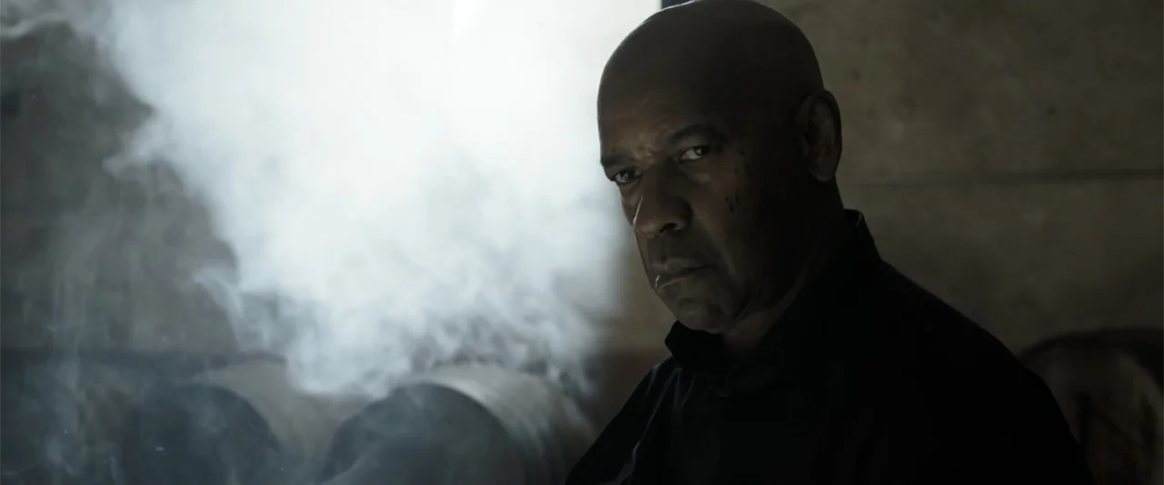 The Equalizer 3 (2023) movie still: closeup — A dark, dimly lit room is filled with thick white smoke and shadows. A bald man wearing a black shirt…