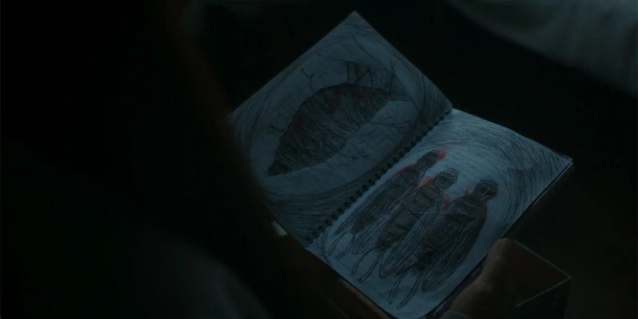 Nokturno (2024) movie still: closeup — A dimly lit room provides a dark environment for a person to examine a sketchbook. The notebook is held open…