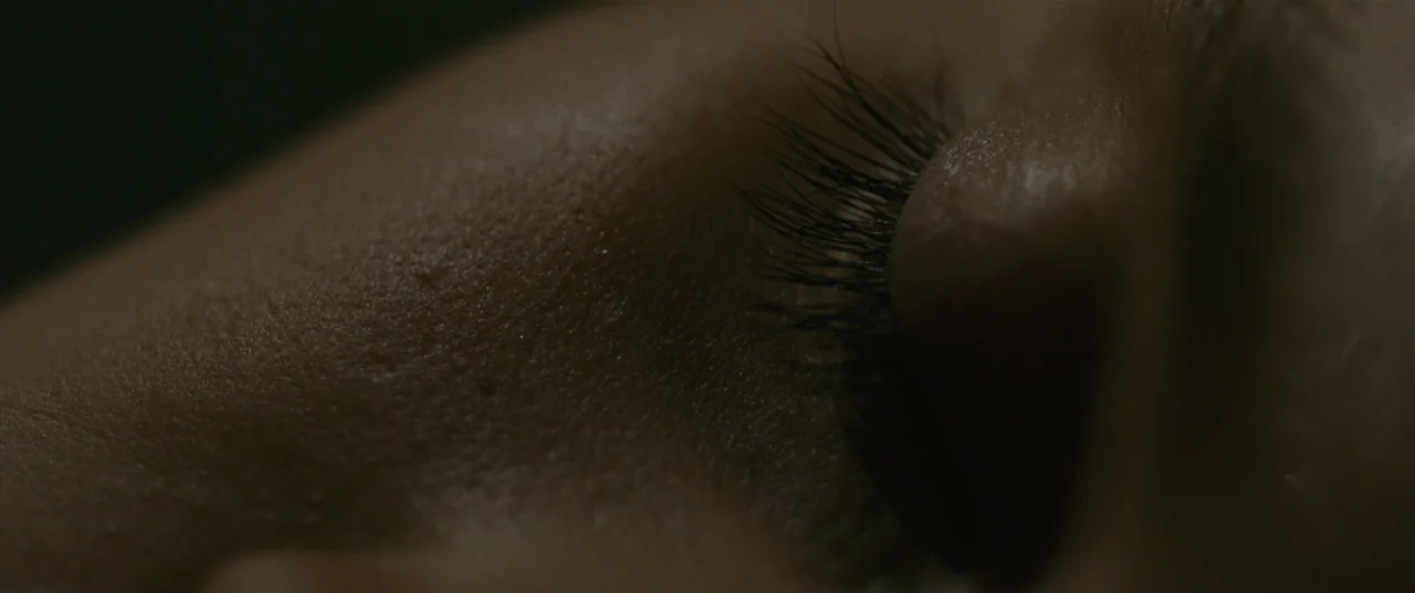 Evolution (2015) movie still: closeup — A close-up of a human face in extreme low light. A closed eye with visible lashes is the central focus.