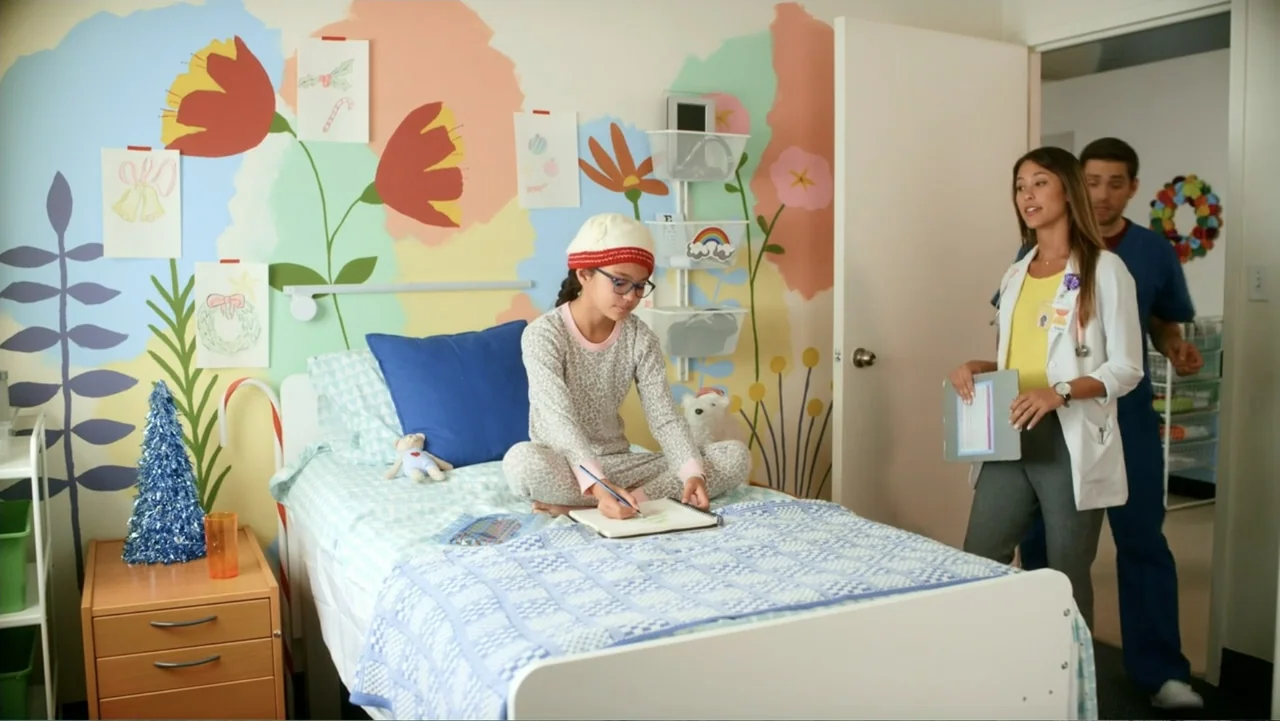Christmas with a Prince (2018) movie still: medium — A hospital room features a wall painted with a vibrant floral mural and child artwork. A young…