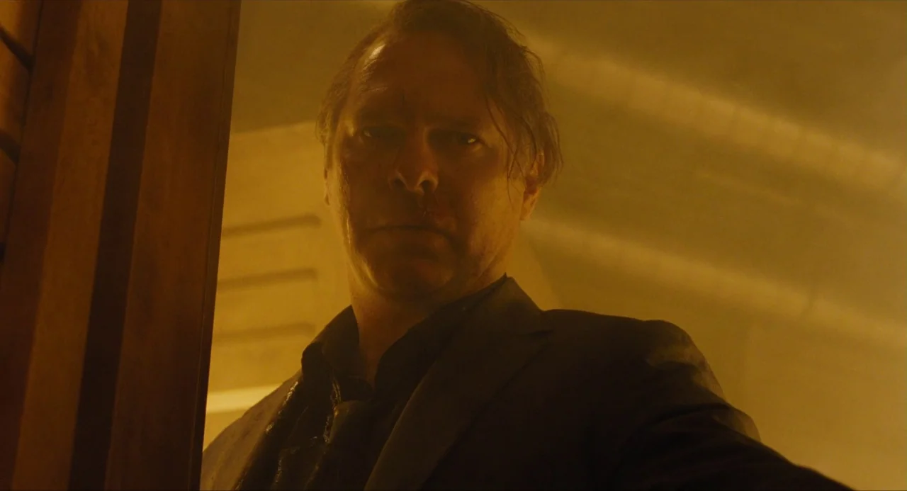 Snowpiercer (2013) movie still: medium — A dimly lit narrow corridor features warm, hazy light against a solid wall. A middle-aged man in a dark…