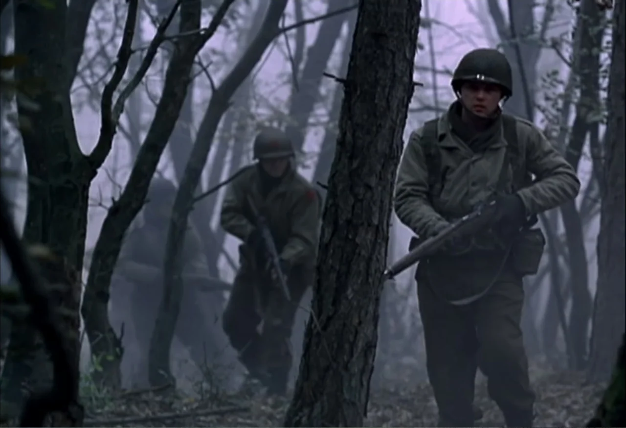When Trumpets Fade (1998) movie still: fullbody — Soldiers in 1940s combat uniforms walk through a dense, fog-covered woodland area. Three men move…