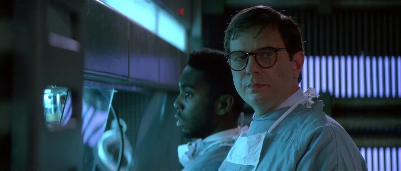Universal Soldier (1992) movie still: medium — A dimly lit, sterile laboratory environment features blue fluorescent overhead lights and equipment.…