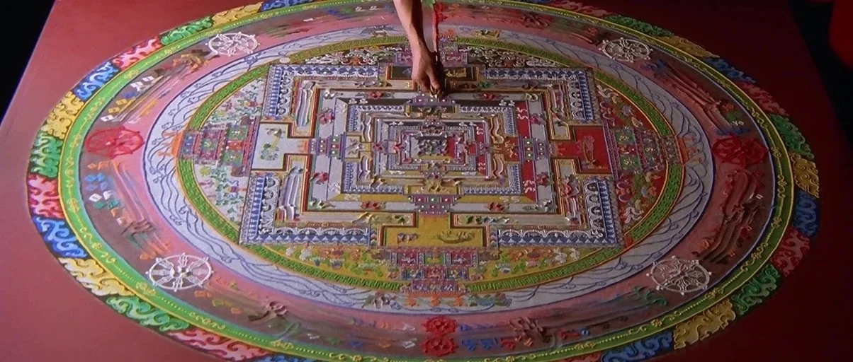 Kundun (1997) movie still: medium — A complex sand mandala is meticulously constructed on a flat table surface. A human hand uses a tool to deposit…
