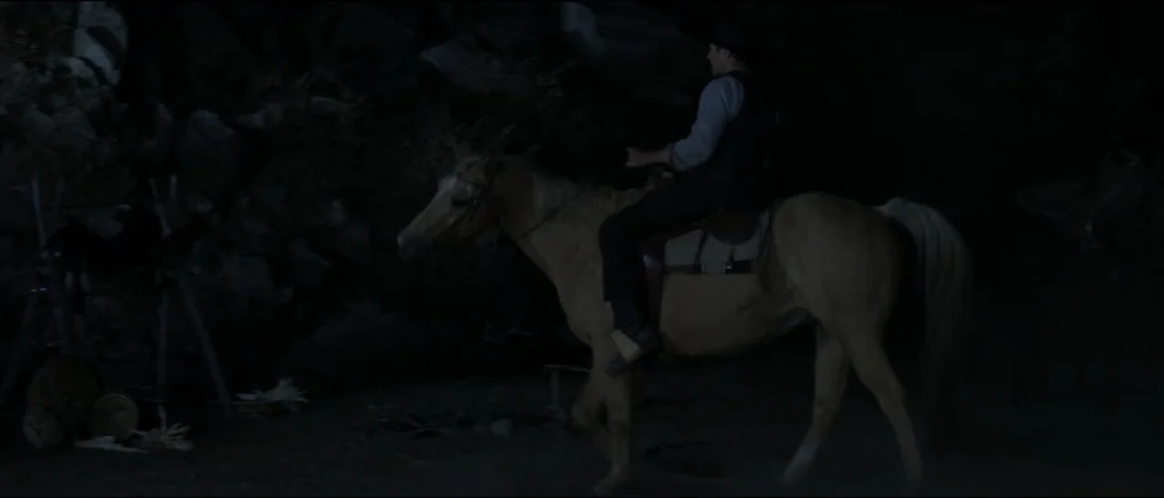 Dead for a Dollar (2022) movie still: medium — A dark, rocky path at night is sparsely lit by dim moonlight. A man in period clothing rides a…