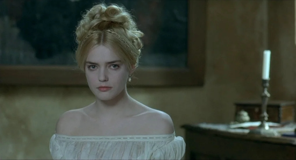 The Last Mistress (2007) movie still: closeup — A dimly lit room features a pale woman in a Victorian-style off-the-shoulder dress. She faces…