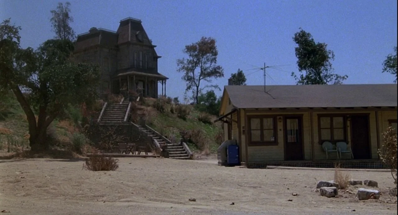 Psycho III (1986) movie still: establishing — A Victorian-style mansion sits atop a grassy hill overlooking a small single-story motel. A sandy lot…